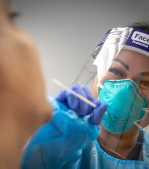 Nurse in PPE administering a nasal swab test.